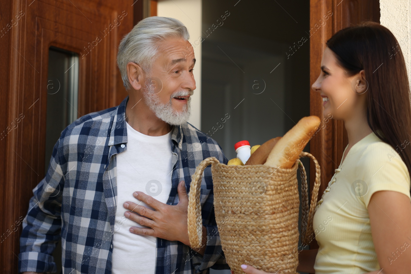 Photo of Helping neighbours. Young woman with bag of products visiting senior man outdoors