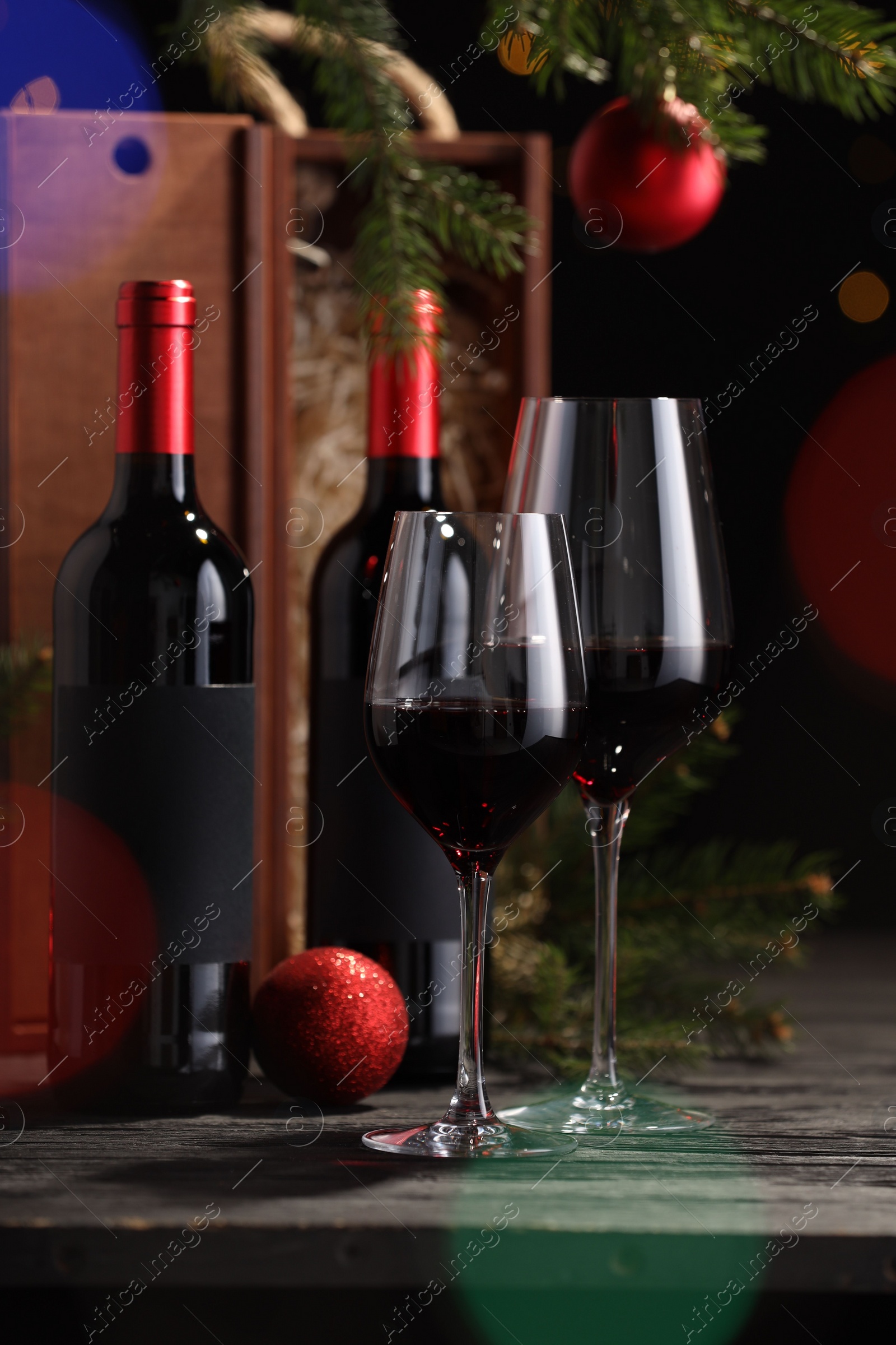 Photo of Bottles of wine, glasses, wooden boxes, fir twigs and red Christmas balls on table