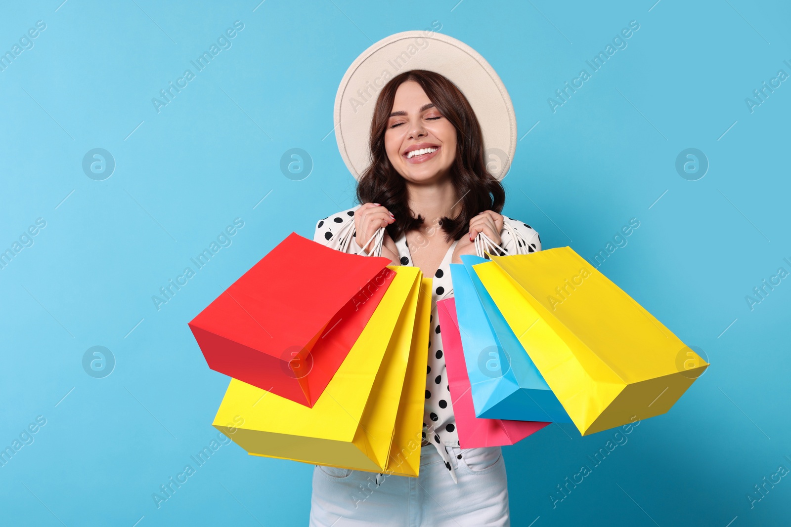 Photo of Beautiful young woman with paper shopping bags on light blue background