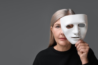 Photo of Multiple personality concept. Woman with mask on gray background, space for text