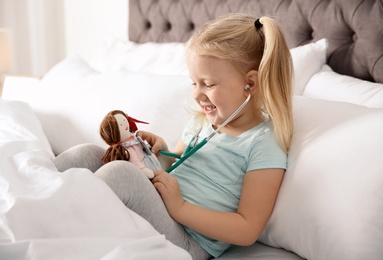 Photo of Cute child imagining herself as doctor while playing with stethoscope and doll at home