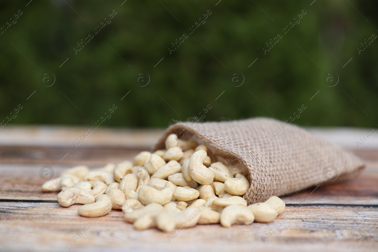 Photo of Tasty cashew nuts and burlap bag on wooden table outdoors, closeup. Space for text