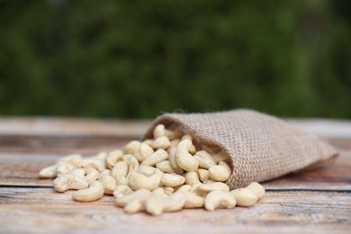 Photo of Tasty cashew nuts and burlap bag on wooden table outdoors, closeup. Space for text