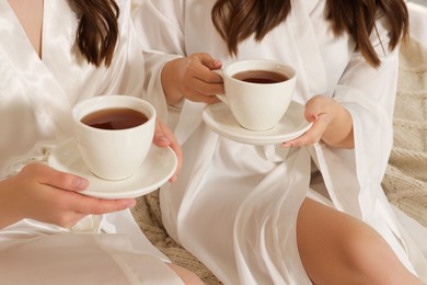 Photo of Bride and her bridesmaid drinking tea at home, closeup. Wedding day