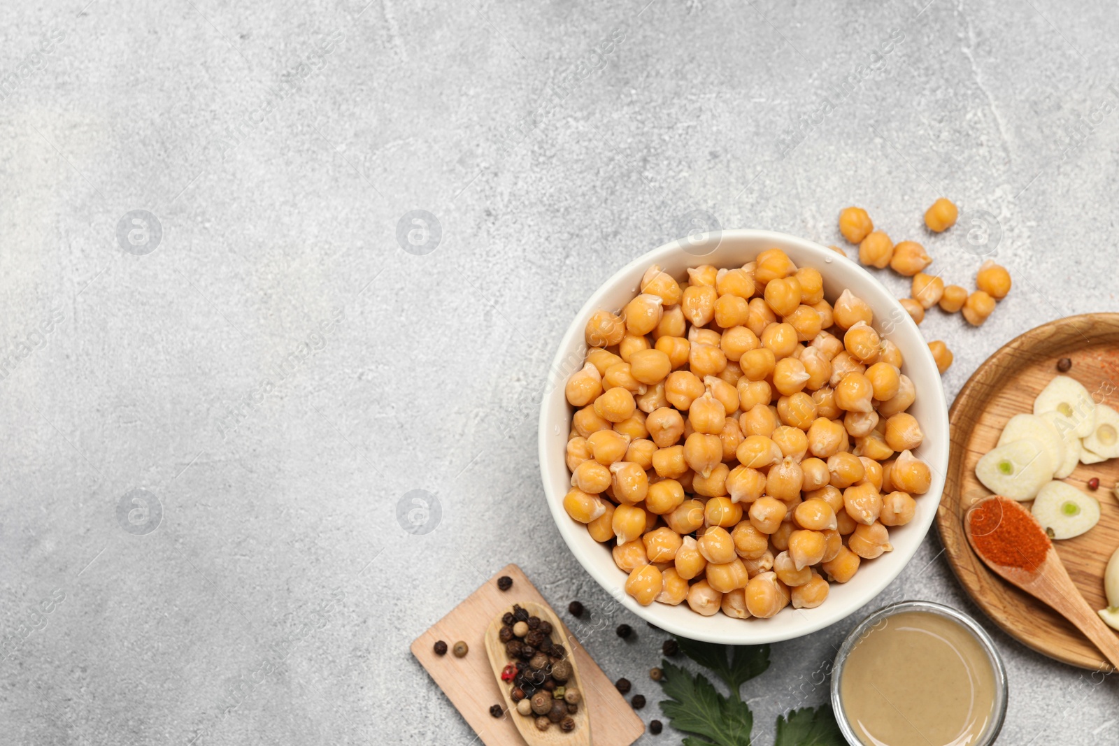 Photo of Delicious chickpeas and different ingredients on light grey table, flat lay with space for text. Cooking hummus