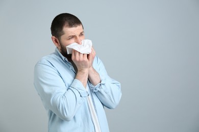 Photo of Man with tissue suffering from runny nose on light grey background. Space for text
