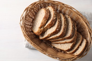 Slices of fresh homemade bread in wicker basket on white wooden table, top view