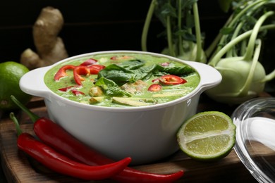 Photo of Saucepan with delicious green curry chicken soup and different ingredients on wooden board