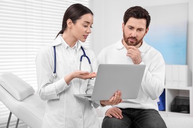 Doctor with laptop consulting patient during appointment in clinic