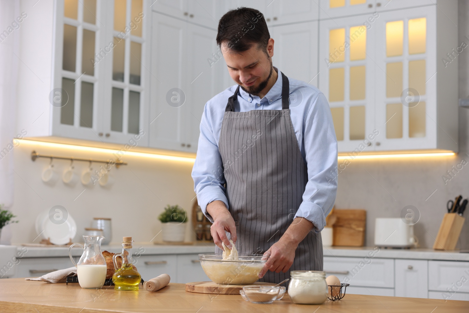 Photo of Making bread. Man preparing dough at wooden table in kitchen