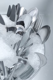 Washing silver spoons, forks and knives in foam, above view