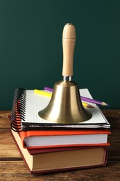 Golden bell, books and pencils on wooden table near green chalkboard. School days