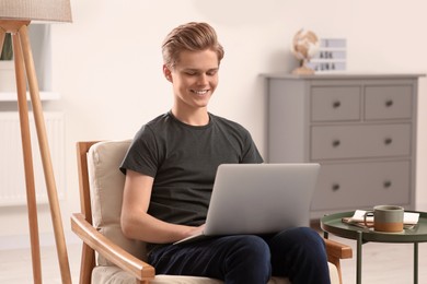 Online learning. Teenage boy with laptop in armchair at home