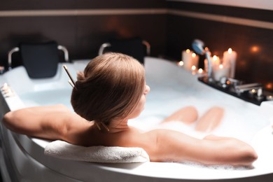Photo of Beautiful woman taking bubble bath indoors, back view. Romantic atmosphere