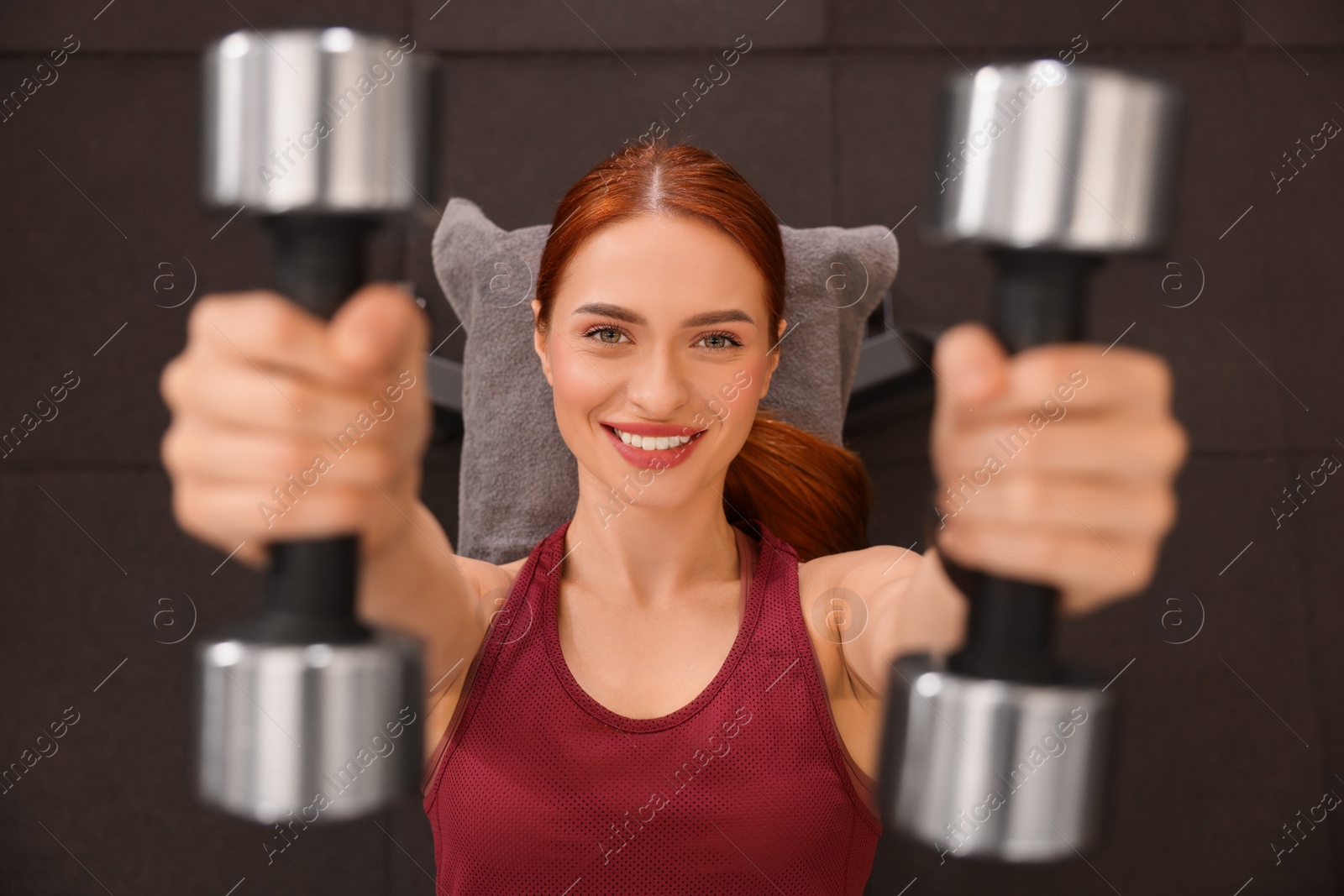 Photo of Athletic young woman doing exercise with dumbbells in gym, top view