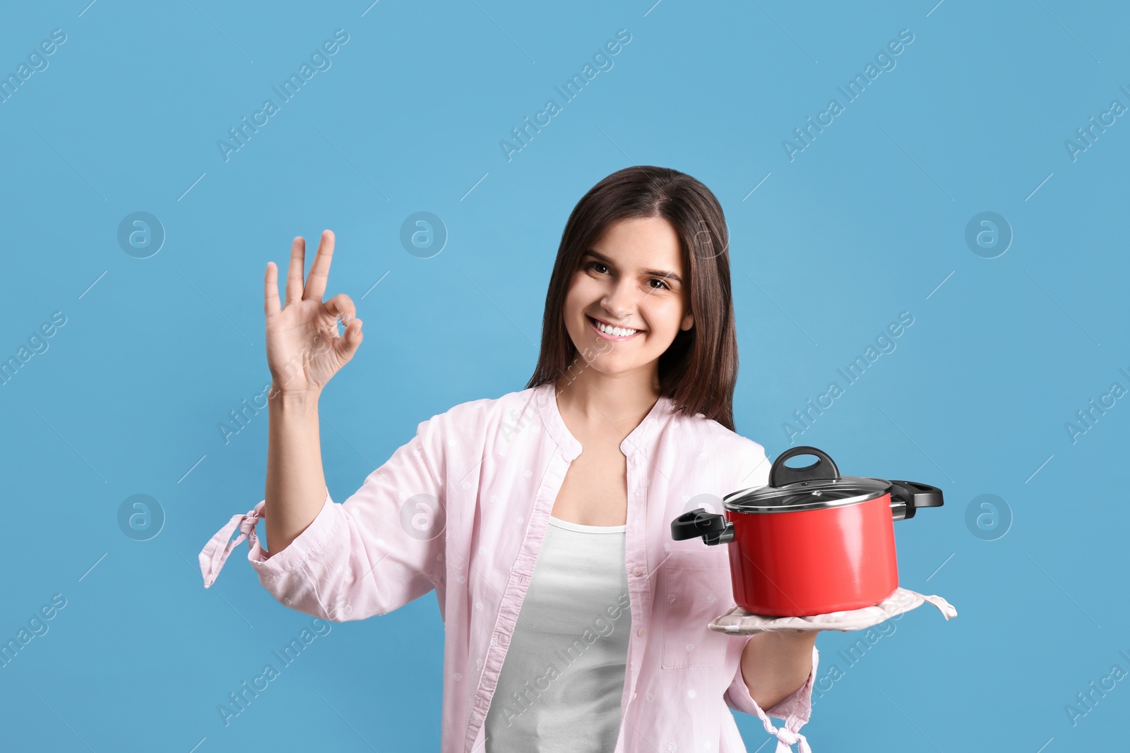 Photo of Happy young woman with cooking pot on light blue background