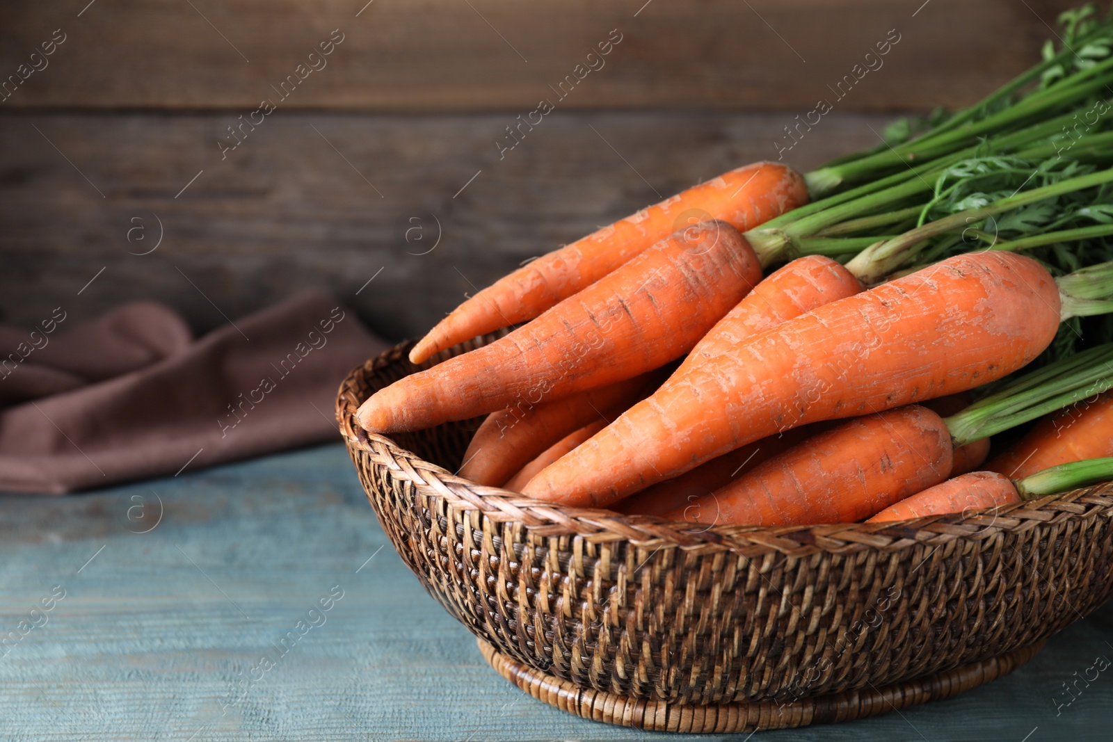 Photo of Fresh carrots in basket on blue wooden table, closeup