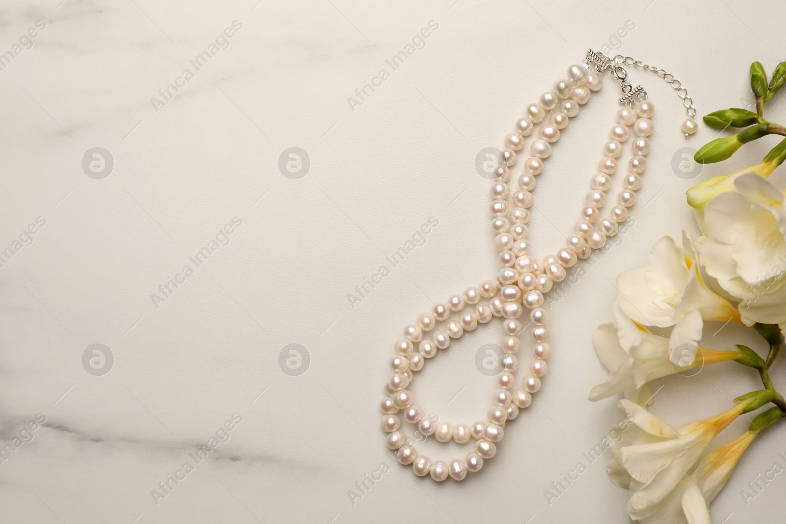 Photo of Beautiful pearl necklace and flowers on white marble table, flat lay. Space for text