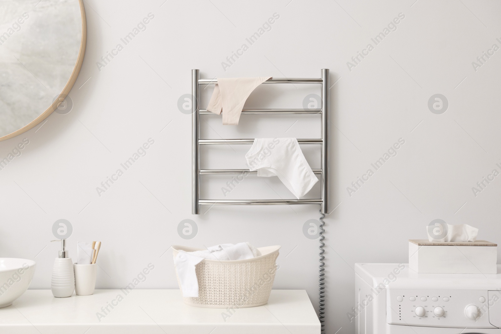 Photo of Heated towel rail with underwear on white wall in bathroom