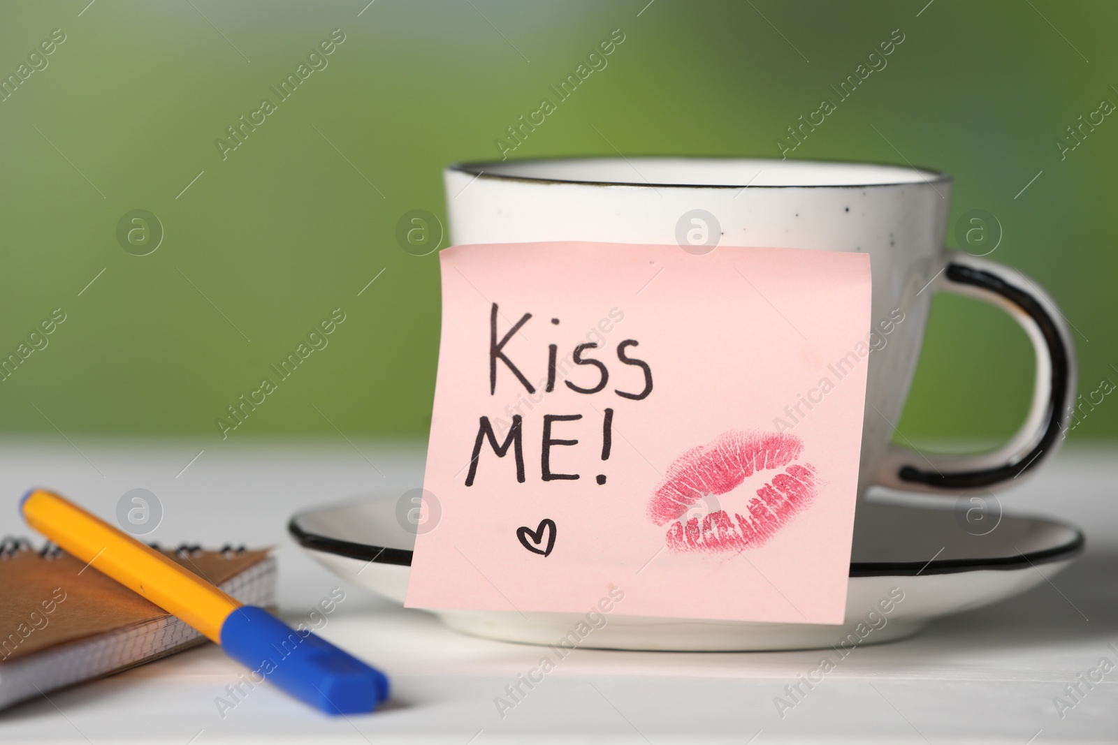 Sticky note with phrase Kiss Me, lipstick mark, cup of drink and notebook on white table against blurred background, closeup Photo of Sticky note with phrase Kiss Me, lipstick mark, cup of drink and notebook on white table against blurred background, closeup