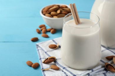 Photo of Glass of almond milk, jug and almonds on light blue wooden table, space for text