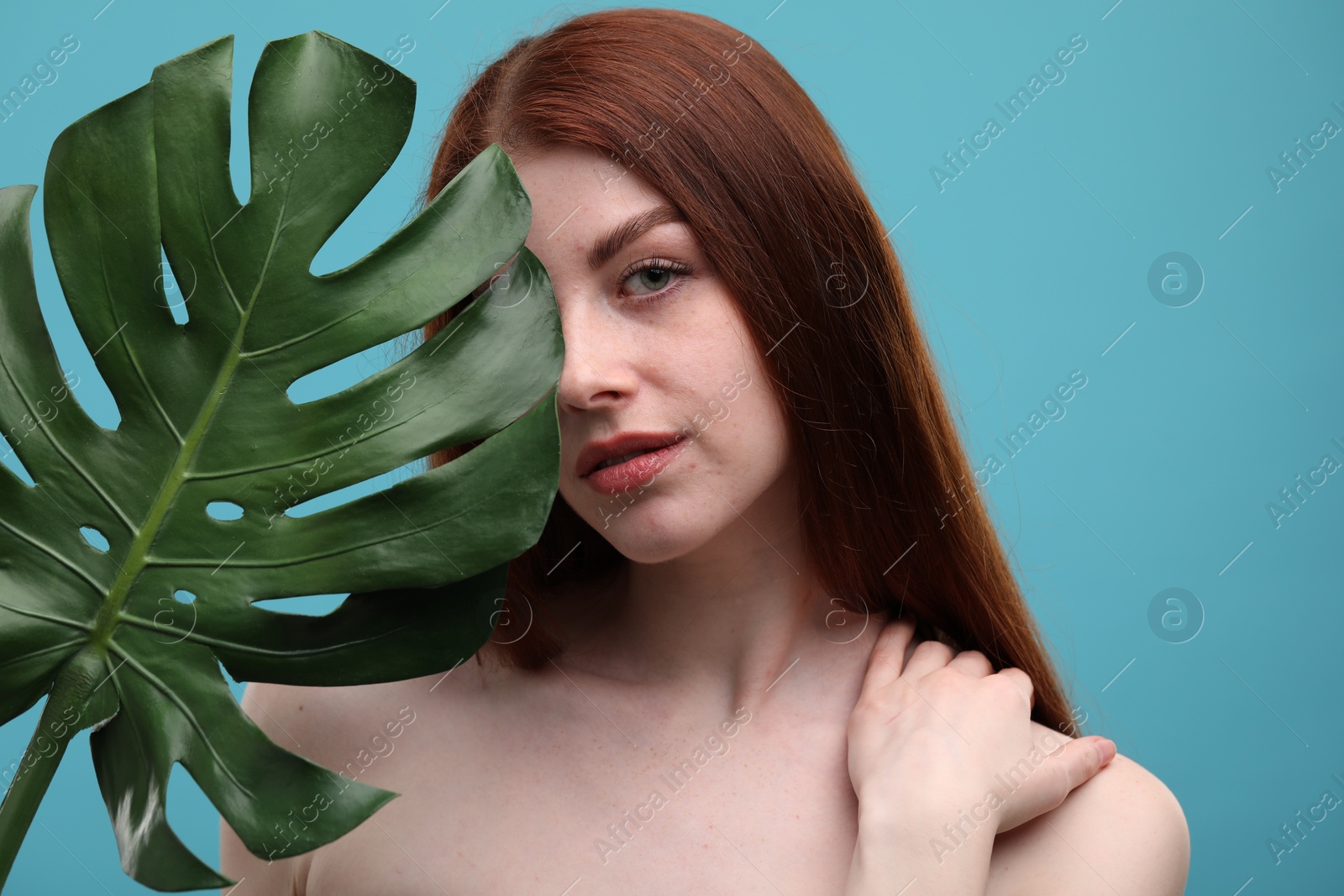 Photo of Beautiful woman with freckles and monstera leaf on light blue background