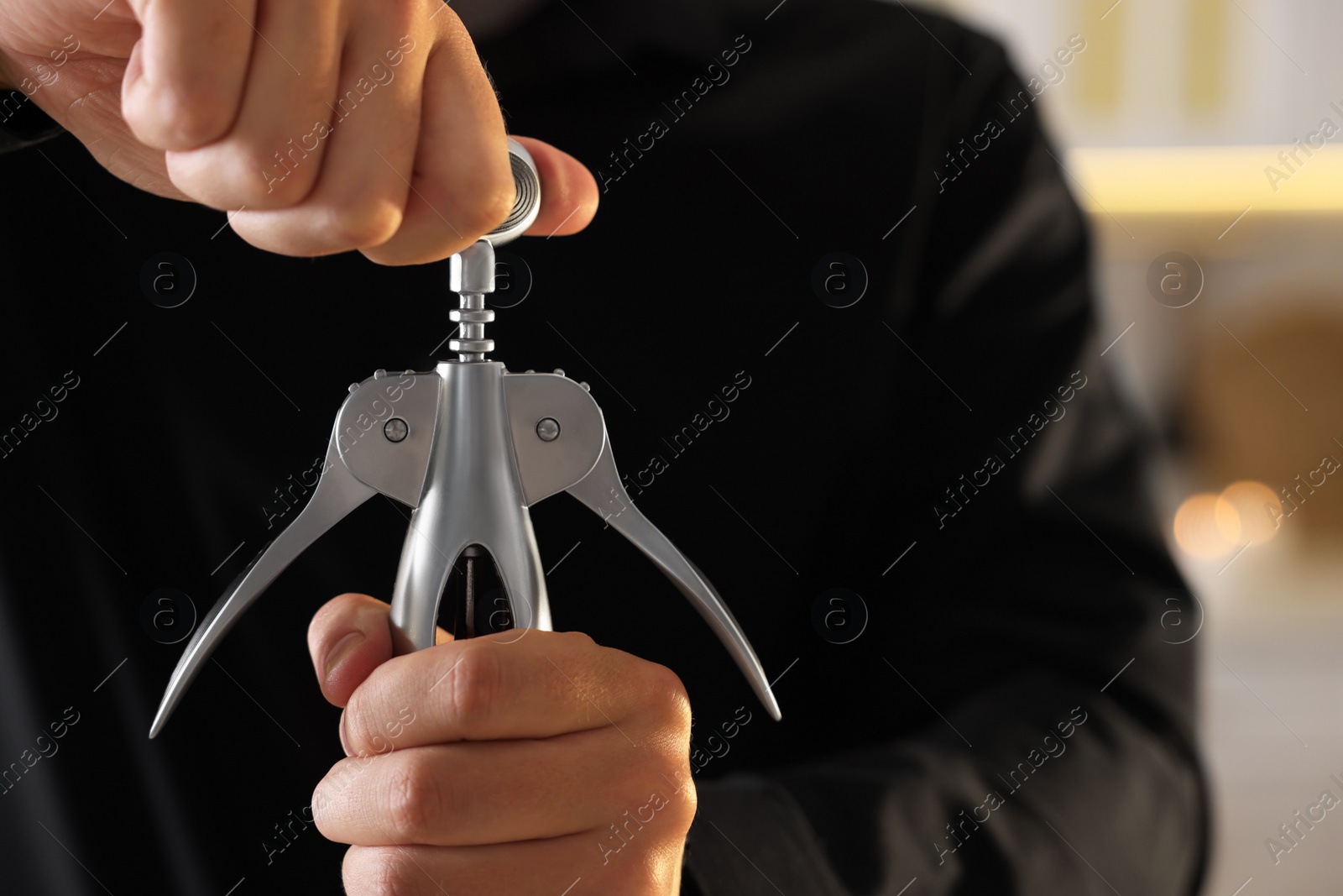 Photo of Man opening wine bottle with corkscrew indoors, closeup. Space for text