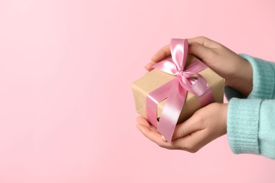Photo of Woman holding gift box with bow on pink background, closeup. Space for text