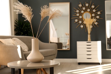 Photo of Vase with dry plants on table in living room. Interior design