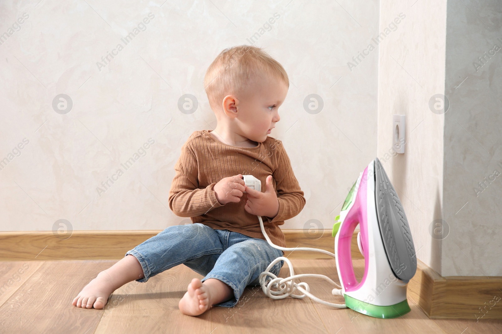 Photo of Little child playing with iron plug near electrical socket at home. Dangerous situation