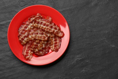 Plate with fried bacon slices on dark textured table, top view. Space for text
