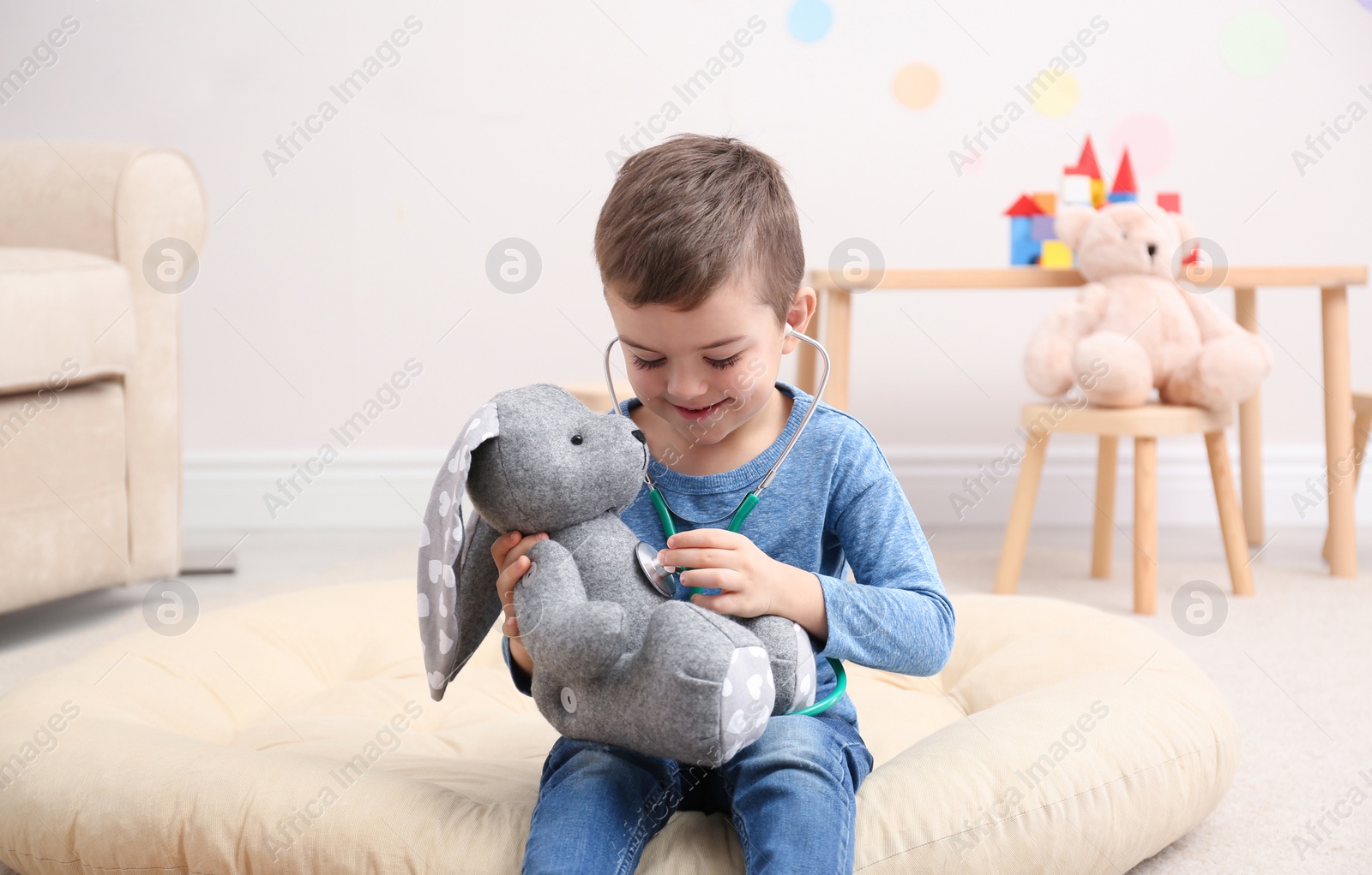 Photo of Cute child playing doctor with stuffed toy on floor in hospital