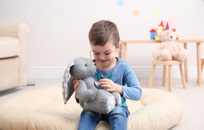 Cute child playing doctor with stuffed toy on floor in hospital