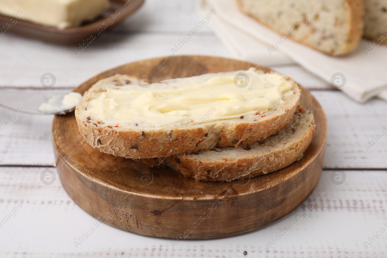 Photo of Slices of tasty bread with butter on white wooden table, closeup