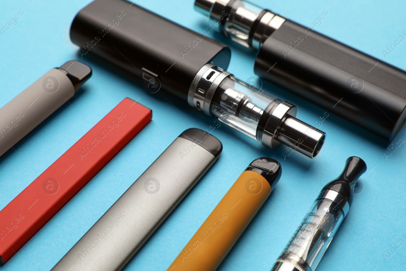 Photo of Different electronic cigarettes on light blue background, closeup