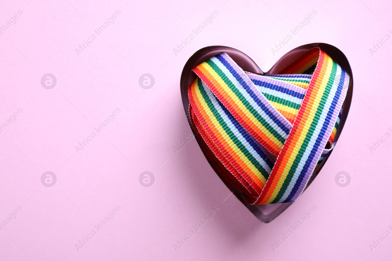 Photo of Heart shaped mold and bright rainbow ribbon on color background, top view with space for text. Symbol of gay community