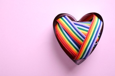 Heart shaped mold and bright rainbow ribbon on color background, top view with space for text. Symbol of gay community