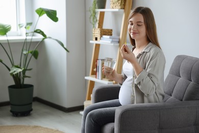 Photo of Beautiful pregnant woman holding pill and glass with water at home