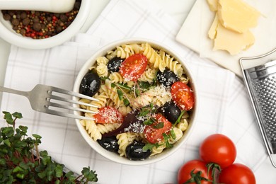 Bowl of delicious pasta with tomatoes, olives and cheese on white table, flat lay
