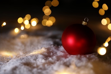 Photo of Christmas ball and fairy lights on white snow outdoors. Space for text