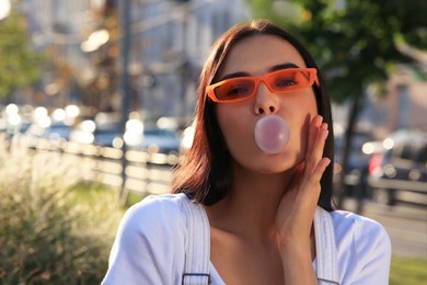 Beautiful woman in sunglasses blowing gum outdoors