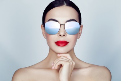 Image of Attractive woman in stylish sunglasses on light grey background. Sky with clouds reflecting in lenses