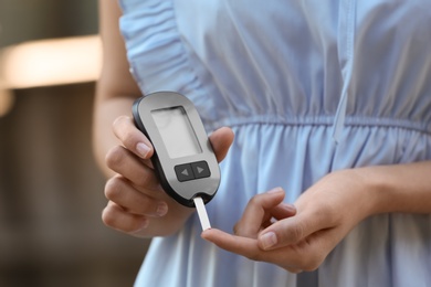 Photo of Woman using digital glucometer on blurred background. Diabetes control