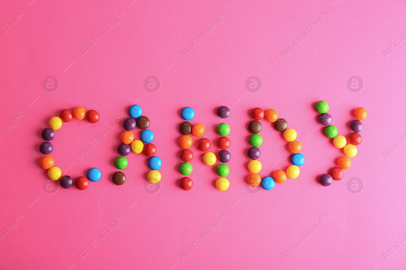 Photo of Word CANDY made of different glazed candies on pink background, flat lay