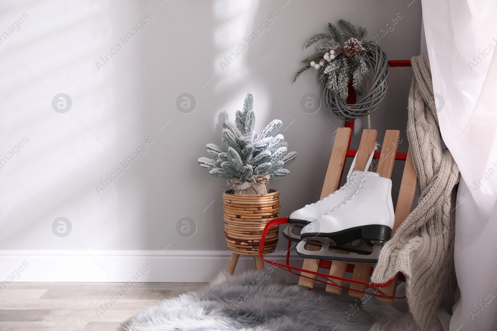 Photo of Pair of ice skates, sleigh and beautiful Christmas decor near white wall indoors, space for text