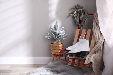 Pair of ice skates, sleigh and beautiful Christmas decor near white wall indoors, space for text