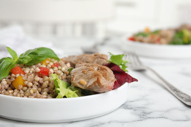 Photo of Tasty buckwheat porridge with meat on white marble table, closeup