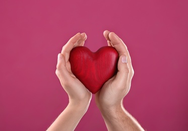 Photo of Man and woman holding decorative heart on color background, closeup