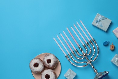 Flat lay composition with Hanukkah menorah and donuts on light blue background, space for text