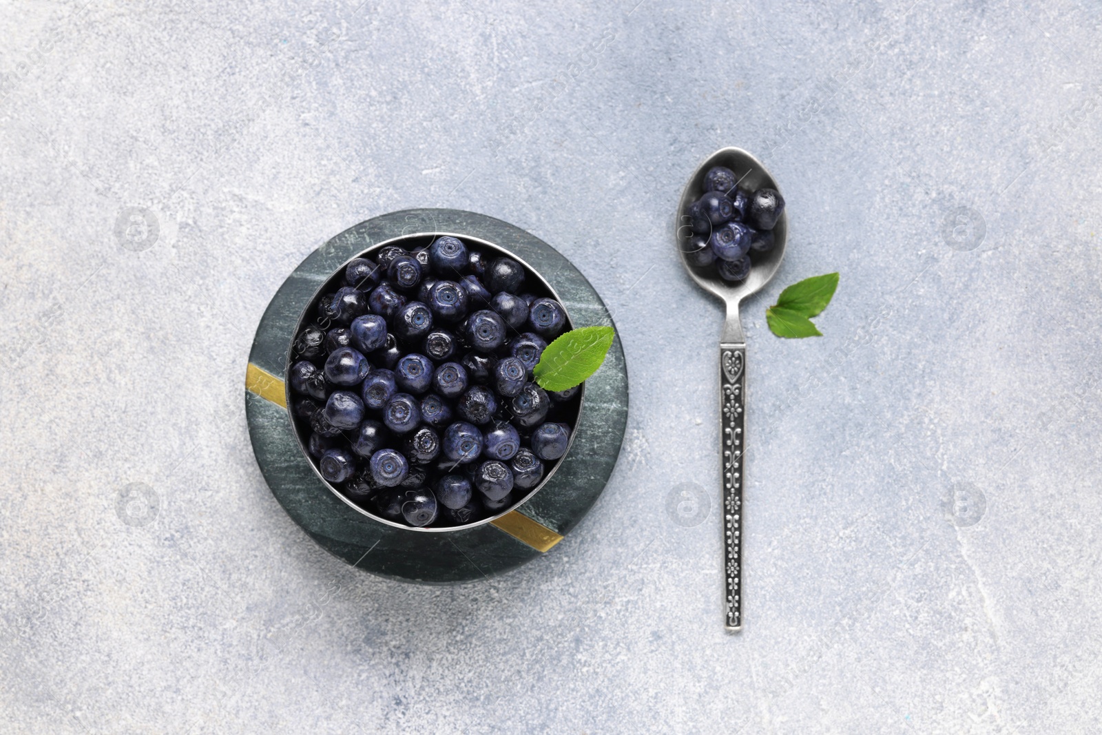 Photo of Ripe bilberries and leaves on light grey textured table, flat lay